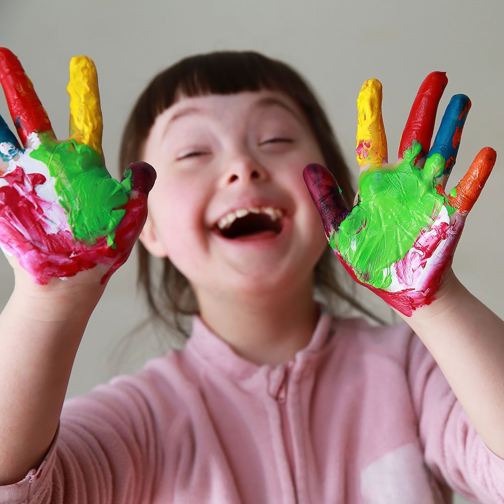 A girl with colourful hands covered in paint, showcasing her artistic side.