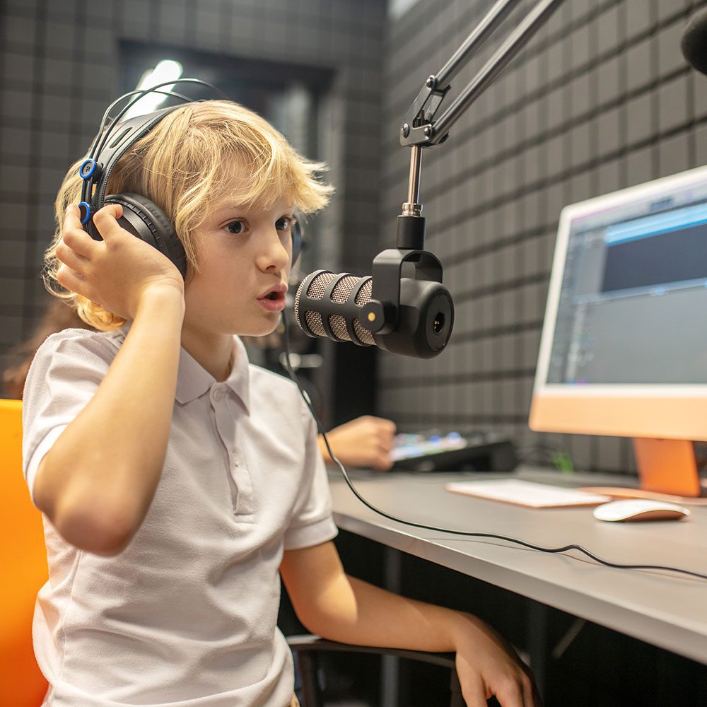 A boy wearing headphones at a microphone in a recording studio.