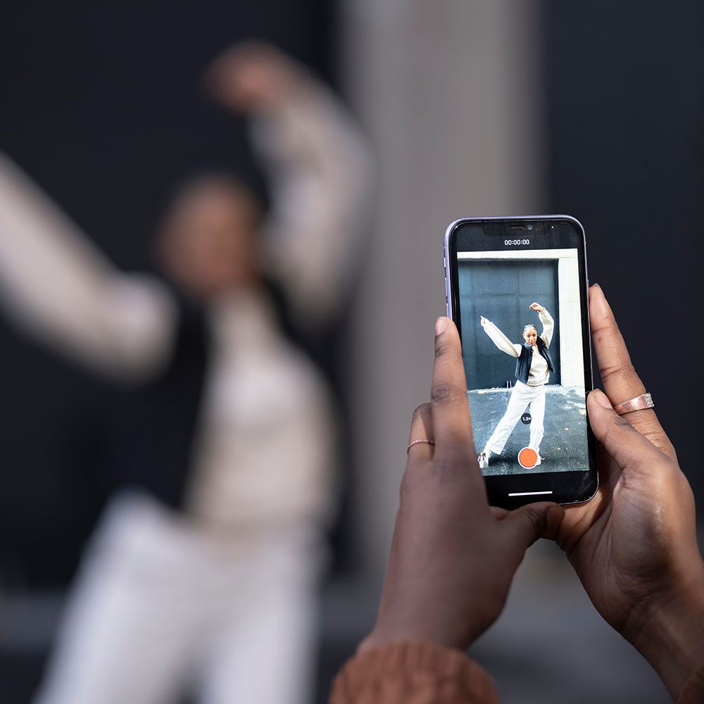 A person capturing a joyful moment as they record video of someone dancing on a smartphone.