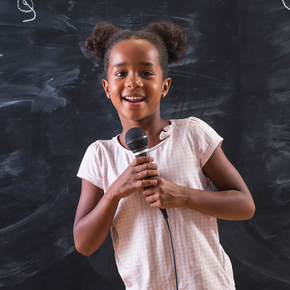 A young girl holds a microphone, ready to sing.